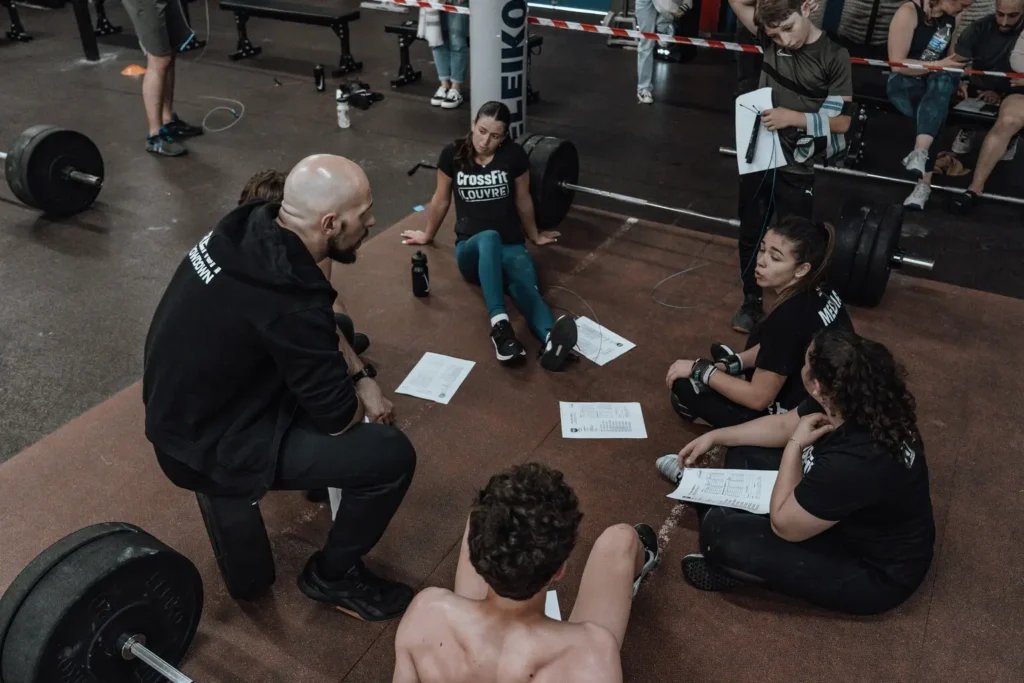 Alunos reunidos no chão da academia discutindo divisão de treino 5 vezes na semana com acompanhamento do coach